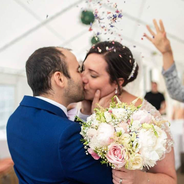 bride and groom kiss holding floral bouquet